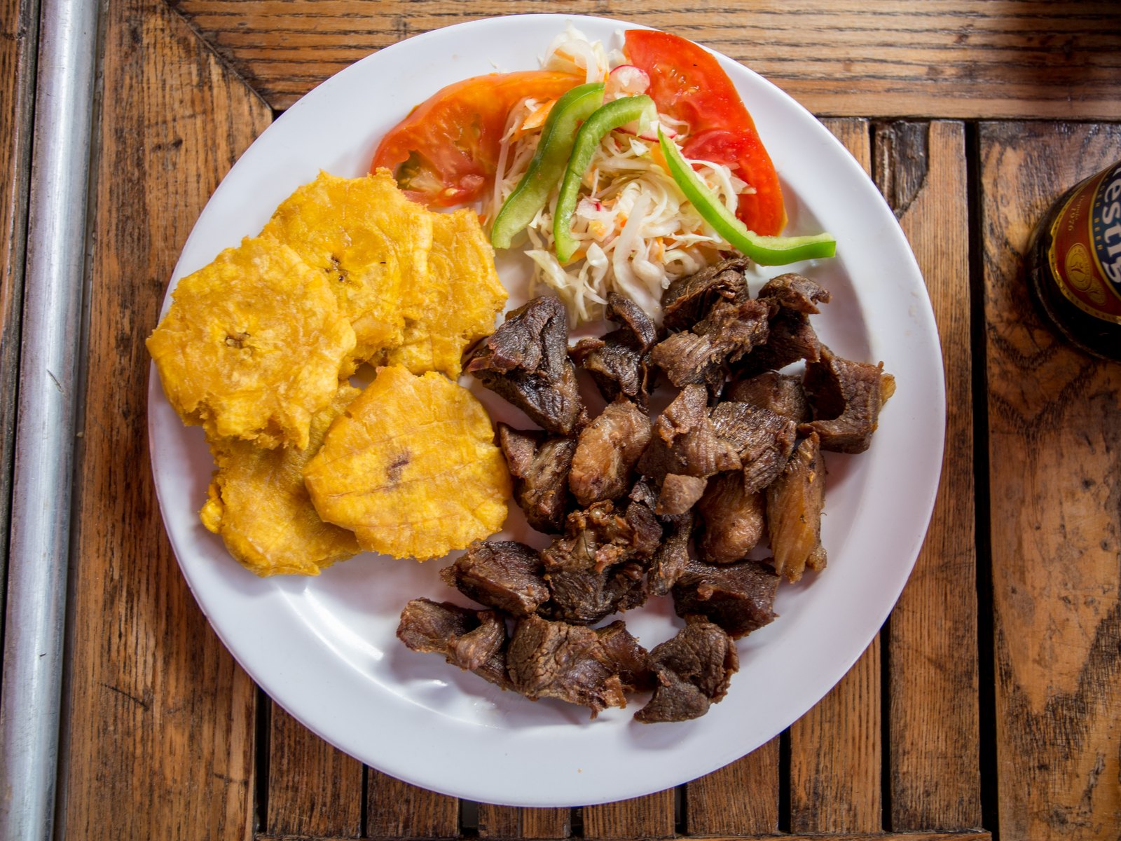 Assiette de griot de porc avec bananes pesées et salade, sur une table en bois